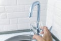 WomenÃ¢â¬â¢s hand lifts the glass to the water jet from the faucet.